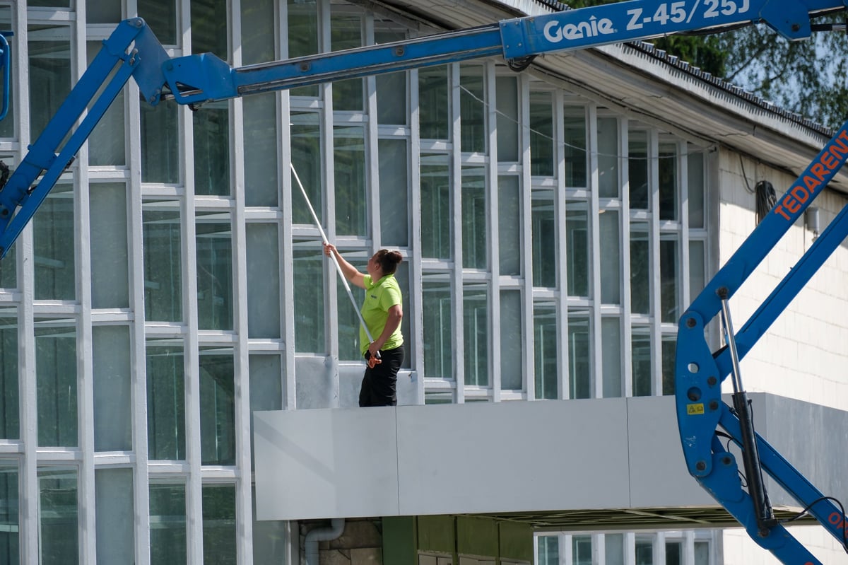 A maintenance worker cleaning the glass facade of a modern building with an extended washing pole