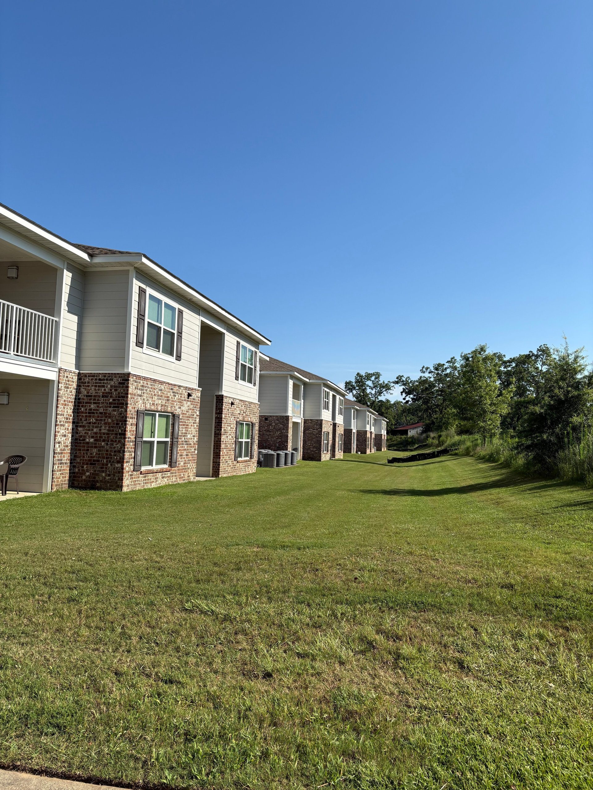 A row of modern brick and tan townhouses with balconies set against a grassy lawn and clear blue sky